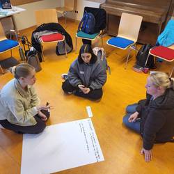 Drei Fachkräfte sitzen auf dem Boden und erarbeiten auf einem Flipchartblatt eine Aufgabe.