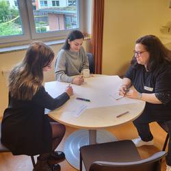 Drei Fachkräfte sitzen an einem runden Tisch und erarbeiten eine Arbeitsaufgabe.
