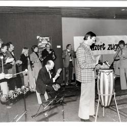 Musiker mit verschiedenen Instrumenten, im Hintergrund ein Banner mit dem Titel "Konzert zugunsten geis..."