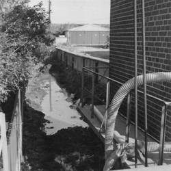 Kanalisation entlang Gebäude, links Gebüsch, rechts hinten ein weiteres Gebäude