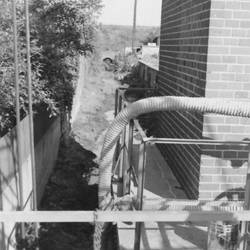 Kanalisation entlang Gebäude, links Gebüsch, rechts hinten ein weiteres Gebäude