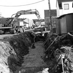 Tiefbauarbeiten im Wohngebiet, links Bagger, rechts Häuser