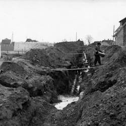 Bauarbeiter verlegt Rohre, im Hintergrund Häuser