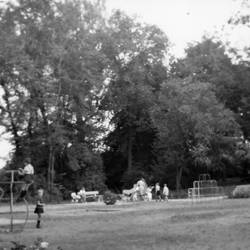 Spielplatz mit Kindern, im Hintergrund Bäume, rechts ein Hinweisschild