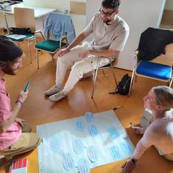 3 Fachkräfte sitzen an einer Flipchart und bearbeiten einen Fall.