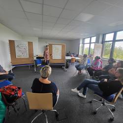 Die Gruppe sitzt im Halbkreis. Eine Teilnehmerin präsentiert ihr Arbeitsergebnis an ihrer Flipchart.