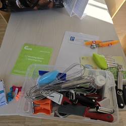 Auf einem Tisch liegt Material aus der Küche. In einer Plastikschale liegen Schneebesen, Sparschäler und weitere Materialien zum Backen.