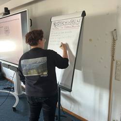 Eine Fachkraft steht an einem Flipchart und sammelt die Ergebnise zum Thema Sprachinseln.