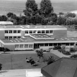 Luftaufnahme einer Schule, davor eine Grünfläche, dahinter Felder