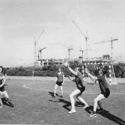 Spiel einer unbekannten Sportart auf einem Sportplatz, im Hintergrund ein Gebäude im Bau