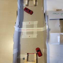 Zwei Schukarton bilden ein Fußballfeld. Je ein Spielauto spielt einen Ball in das gegnerische Tor.