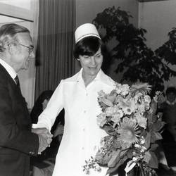 Herr überreicht Dame einen Blumenstrauß, im Hintergrund sitzen unbekannte Personen