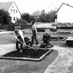 Drei Männer bei Erdarbeiten, im Hintergrund Gebäude