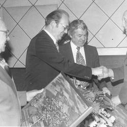 Vier Herren, in der Hand halten sie Luftaufnahmen und Blumensträuße