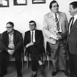 Zwei Herren sitzen auf Stühlen, zwei Herren stehen und geben sich die Hand