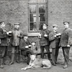 6 Herren mit Bierkrügen vor einem Gebäude, dazwischen ein Kind und ein Hund