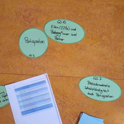 Grundsatz 13 und 7 stehen auf Flipchartblättern. Grundsatz 7 lautet Basisdemokratie: Selbstständigkeit durch Partizipation.