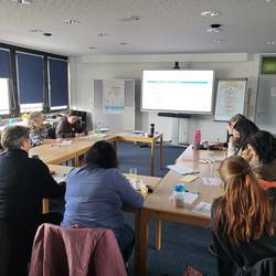 Die Teilnehmenden sitzen in U- Form zum Whiteboard. Es wird Ihnen eine Power Point Präsentation gezeigt.