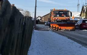 Ein LKW mit einem Schneeschild schiebt Schnee auf einer verschneiten Fahrbahn zur Seite.