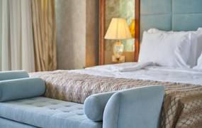 Luxuriöses Hotelbett mit türkiser Chaiselongue im Vordergrund
