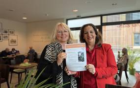 Zwei Frauen stehen nebeneinander und halten einen Ausdruck des Newsletters in die Kamera.