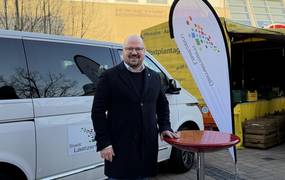 Ein Mann steht auf einem Platz neben einer Beachflag und einem Stehtisch.