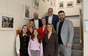 Fünf Frauen stehen neben drei Männern auf einer Treppe. Alle lächeln in die Kamera.