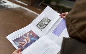 Eine Frau betrachtet eine Zeitschrift. Im Hintergrund Asphalt und etwas Schnee.