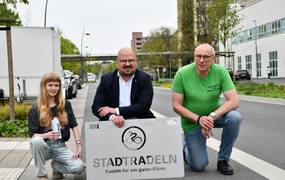 Werbebild mit zwei Männern und einem Mädchen und einem STADTRADEL Schild.