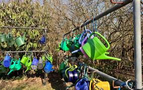 An einer Eisenstange sind bunte Gießkannen mit Schlössern befestigt.