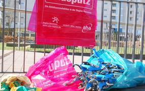 Einige rote Mülltüten und Müllzangen liegen an einem Metallzaun.