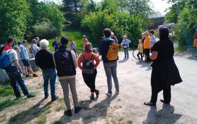 Eine Gruppe von Personen stehend im Kreis, die sich unterhalten. Im Hintergrund grüne Büsche und Gras.