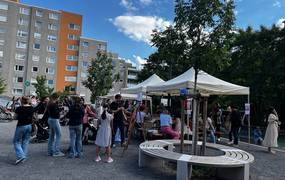 Viele Personen auf einem Fest. Pavillons mit Aktionen zur Teilnahme. Hochhäuser im Hintergrund.