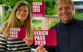 Eine Mitarbeiterin und ein Mitarbeiter des Kinder- und Jugendbüros halten Flyer mit dem Programm des Ferienpasses in die Kamera.