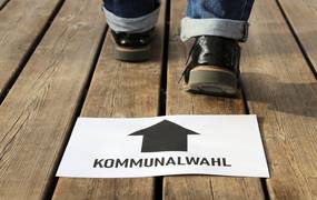 Ein weißes Blatt Papier mit der Aufschrift Kommunalwahl und Füsse, die dahinter stehen.