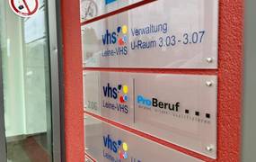 Eine rote Wand mit Hinweisschildern der Leine VHS.