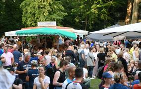 Viele Personen, die auf einer Wieser unter Sonnenschirmen sitzen.