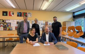 Bürgermeister Kai Eggert und Planerin Kristina Gronau unterzeichnen in einem Klassenraum den Vertrag zur Sanierung des C-Trakts der Albert-Einstein-Schule. Hinter ihnen stehen weitere Vertreterinnen und Vertreter von Schule und Stadtverwaltung.