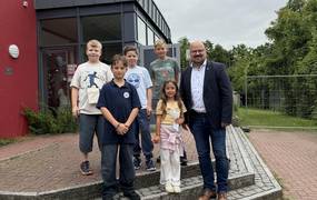 Kinder und ein Mann stehen vor einem Gebäude auf Stufen.