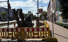 Gelbe Baustellenbaken sperren eine Baustelle ab, auf der bereits ein Bagger steht.