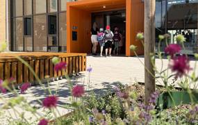 Grundschülerinnen und -schüler betreten mit Schulranzen auf dem Rücken einen orangenen Eingangsbereich einer Schule.