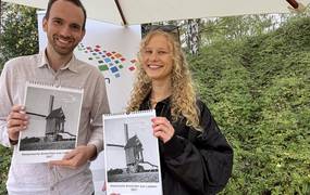 Ein Mann und eine Frau stehen vor einem Sonnenschirm und halten jeweils einen Kalender in die Kamera.