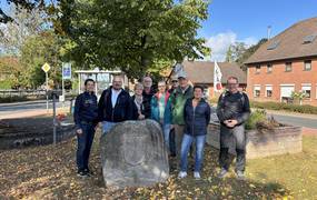 Eine Gruppe von Menschen stehen gemeinsam mit Bürgermeister Kai Eggert in Ingeln-Oessels vor einem großen Stein mit Gravur.