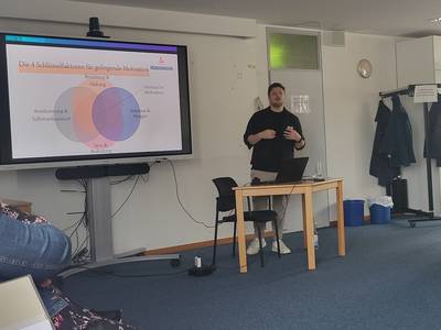 Der Referent Sebastian Lisowski steht vor einem interactiven Whiteboard und präsentiert seine Präsentation.