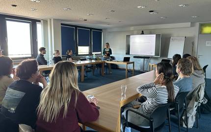 Präsentation der Sprachexpertinnen © Maike Waßmann Die Referentin Maike Waßmann steht am Whitboad und präsentiert eine Powerpoint. Die Fachkräfte sitzten in U- Form zur Präsentation.