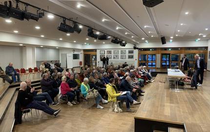 Viele Menschen sitzen in Stuhlreihen und gucken zu eienr Bühne