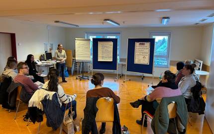 Eröffnung der Veranstaltung © Karen Schlote/Stadt Laatzen Die Teilnehmenden sitzen im Halbkreis auf Stühlen. Die Referentin Marlene Schneider begrüßt den Fachtag. Sie steht vor den Teilnehmenden.