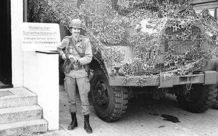 Bewaffneter Soldat neben Militärfahrzeug, daneben Schild mit Aufschrift "Militärischer Sicherheitsbereich"