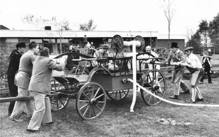 Männer bedienen historische Feuerwehrspritze auf Rasenplatz