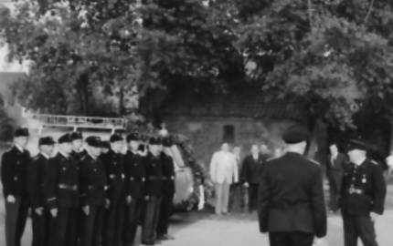 Vermutlich Parade der Feuerwehr, im Hintergrund Feuerwehrfahrzeug mit Leiter